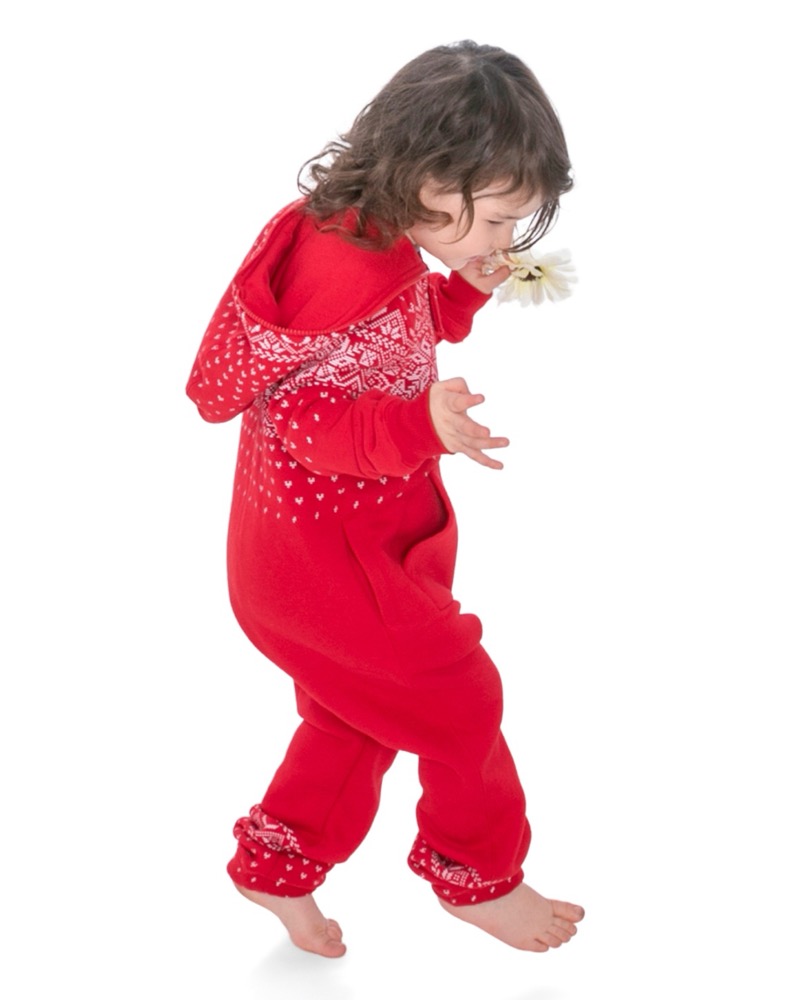 A barefoot toddler in a red hooded onesie mid-stride, holding a daisy, against a plain white background.